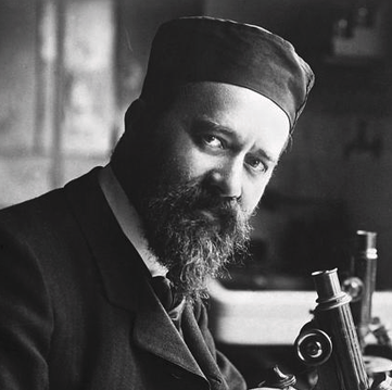 portrait en noir et blanc d'un barbu assis à son miscroscope