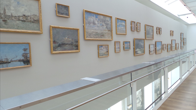 Un. mur avec plein de petits tableaux accrochés comme dans un nuage, les tableaux sont peints par Eugène Boudin)