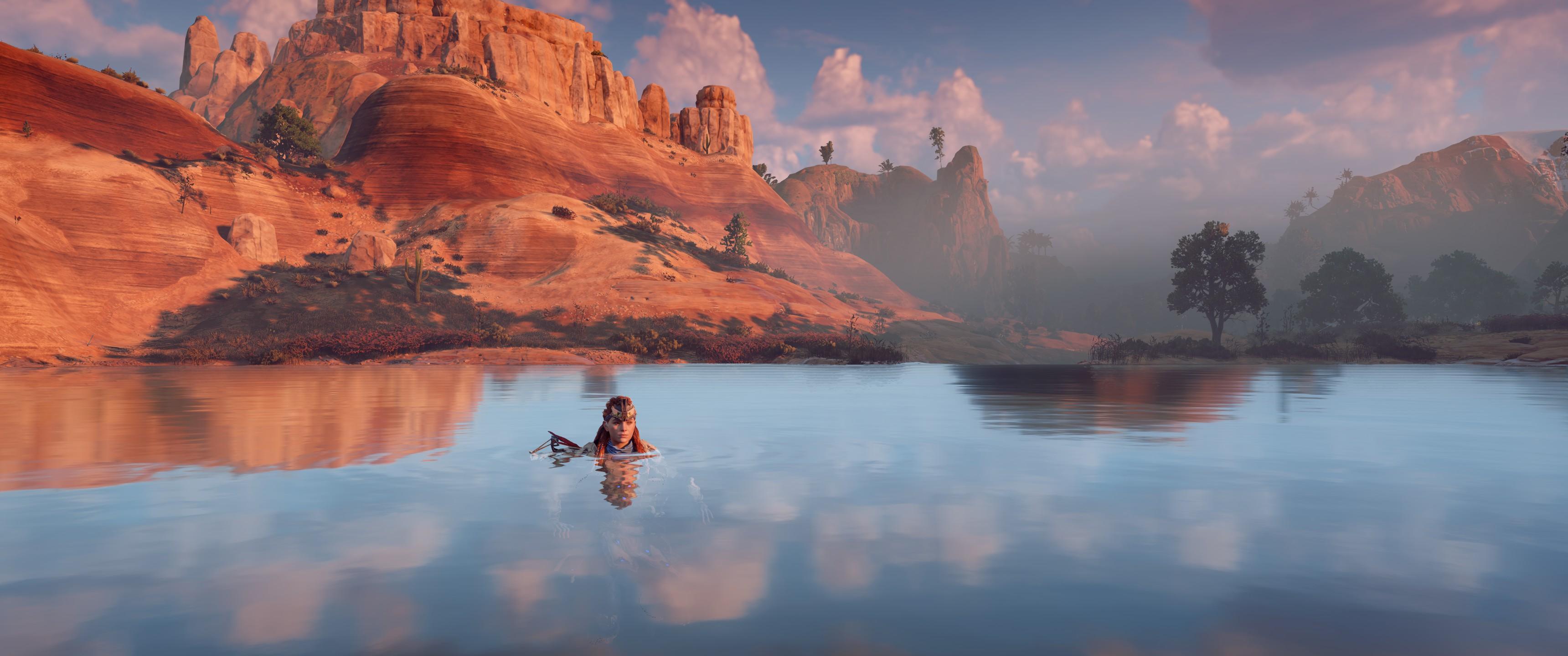 Aloy nage dans un lac. Les reflets de montagnes qu'on voit dans le lac ne correspondent pas du tout au montagne qu'on voit à l'horizon.